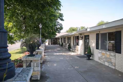 Single-story senior living facility exterior featuring a long walkway, windows, and decorative planters.