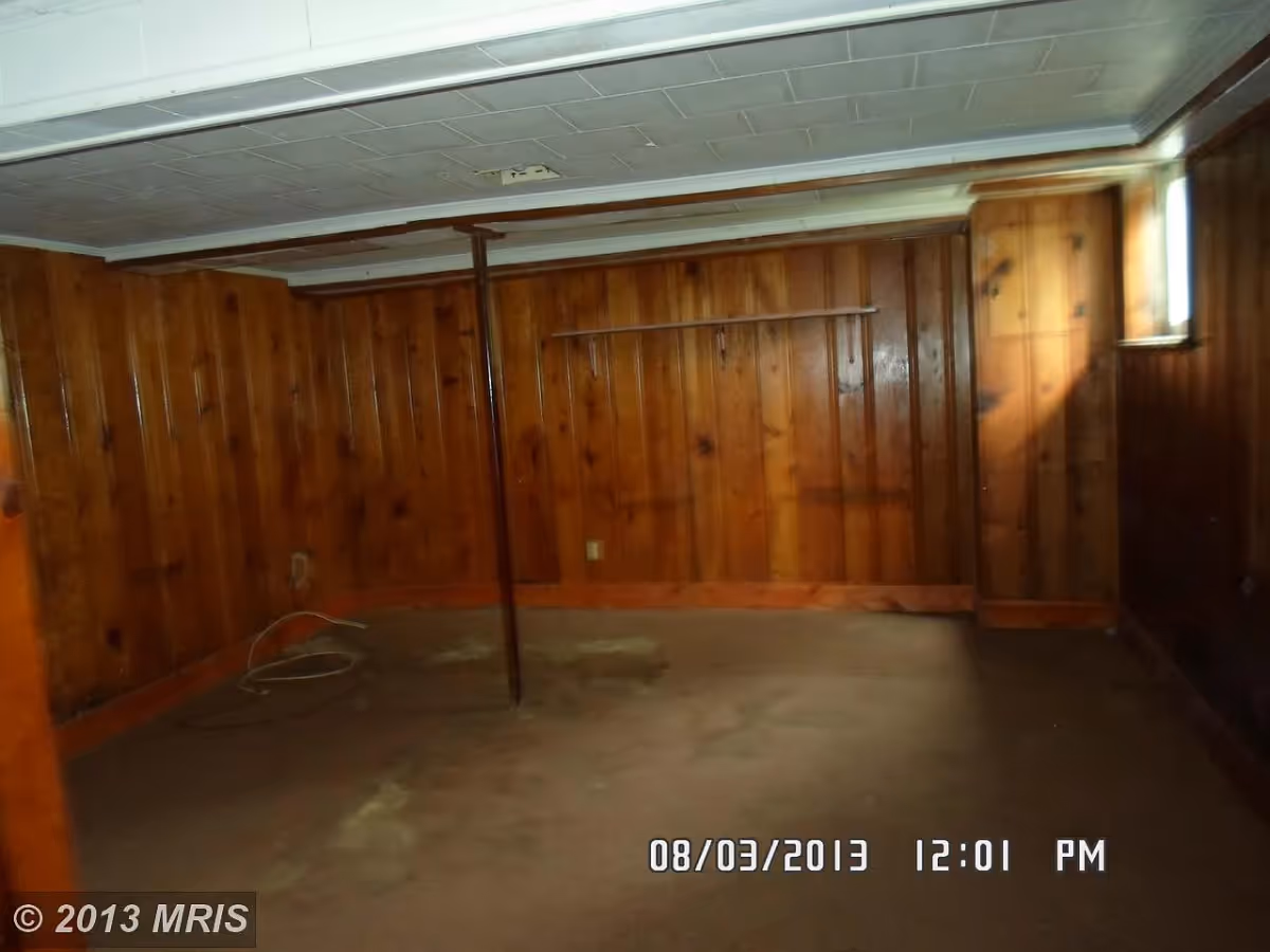 Empty wood-paneled basement room with a central support pole, small window, and carpeted floor.