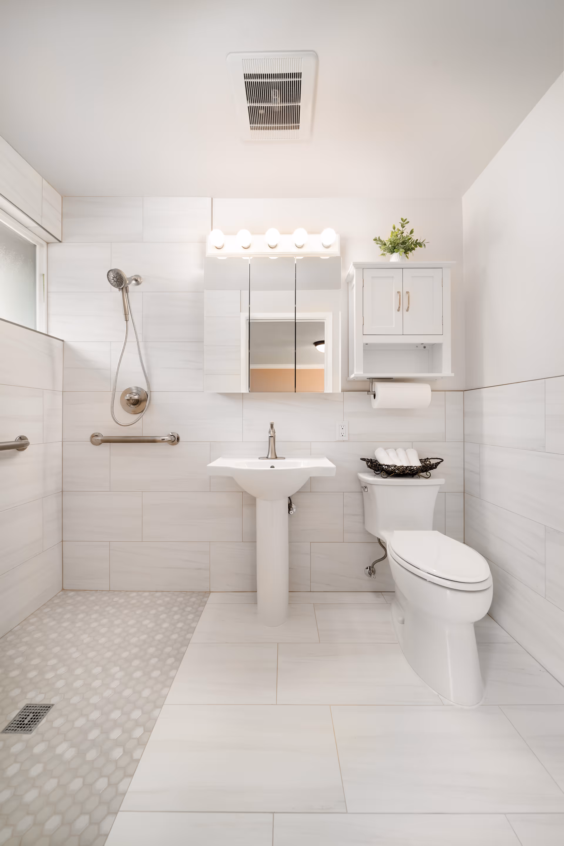 Bright accessible bathroom with a walk-in shower, pedestal sink, toilet, and a wall-mounted medicine cabinet.