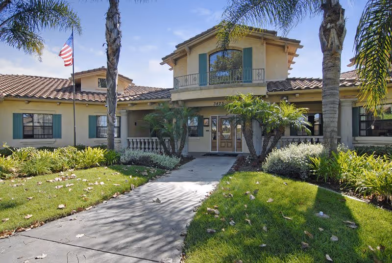 Morning Pointe of Richmond's beige, two-story building with a walkway and palm landscaping.