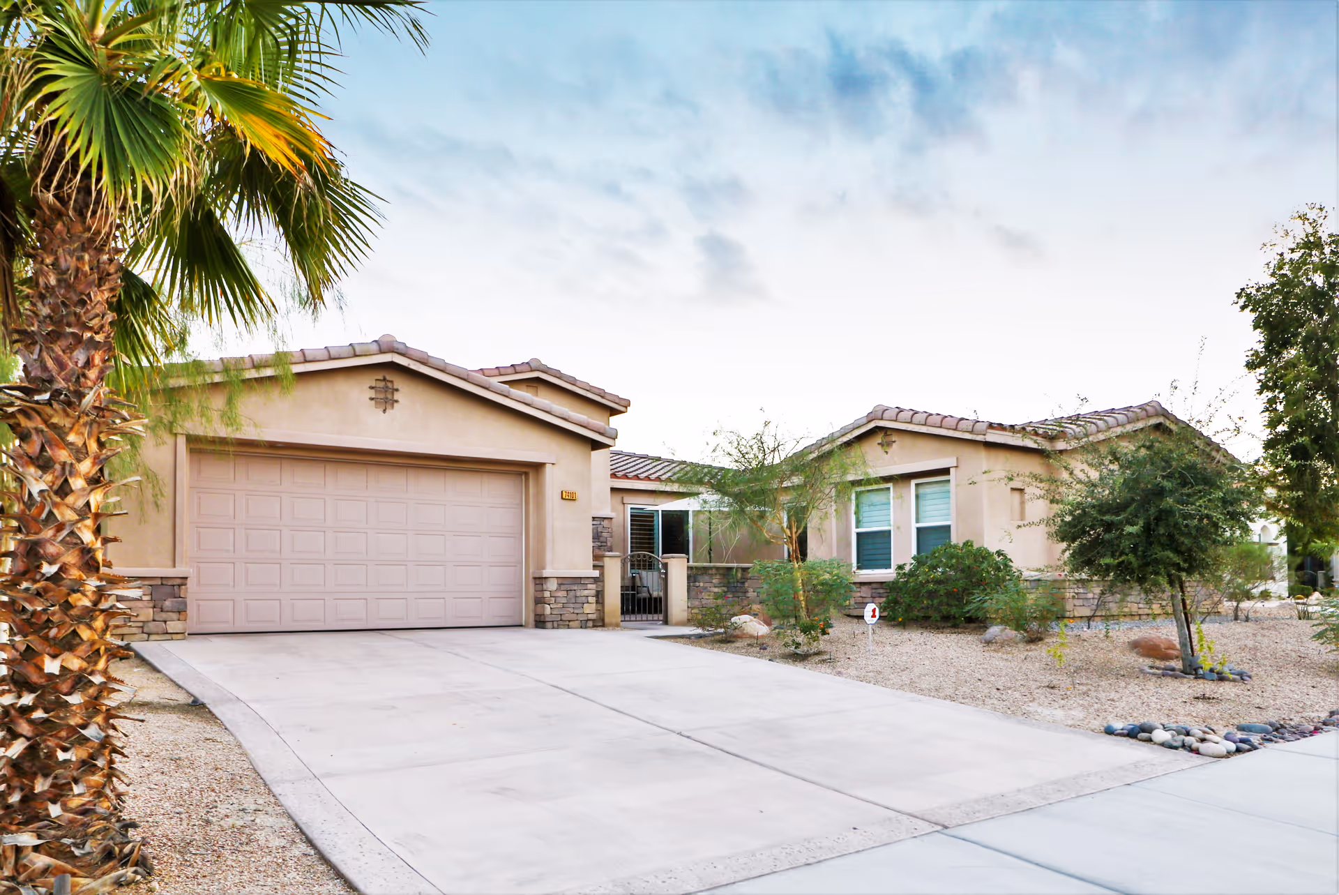 Single-story stucco house with a two-car garage, palm tree, and desert landscaping in front.