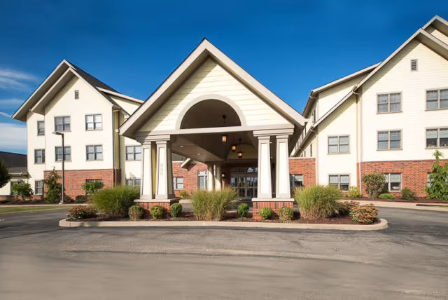 Covered entrance (porte-cochère) of a multi-story senior living building with brick and siding facade and landscaped beds.
