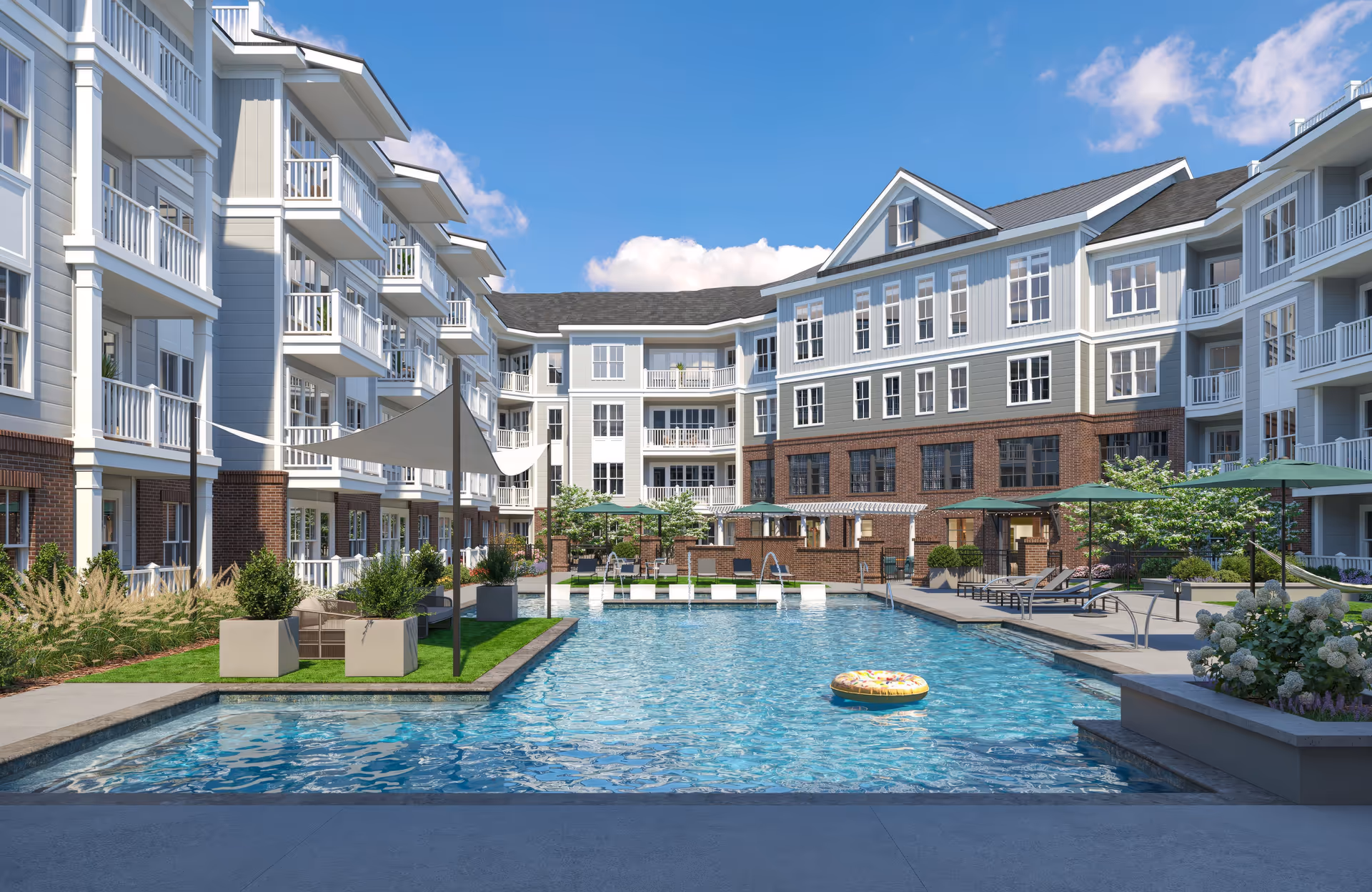 Outdoor swimming pool area at a senior living facility with lounge chairs, umbrellas, and a donut-shaped pool float. Surrounding the pool are multi-story residential buildings with balconies and landscaped greenery under a blue sky with some clouds.