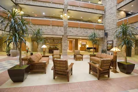 Bright interior lounge with brown cushioned seating, plants, and multi-level balconies.