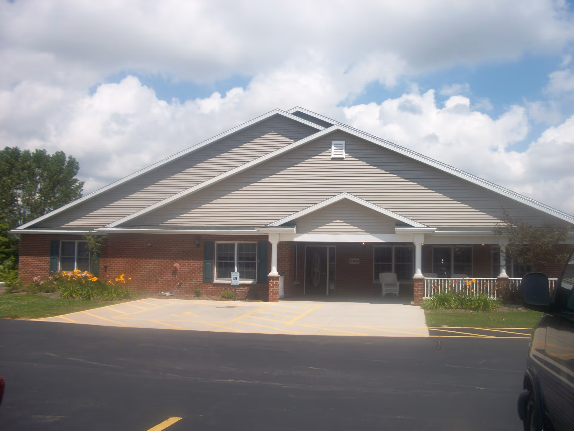 Front exterior of a single-story senior living building with a covered entrance, parking and landscaping.