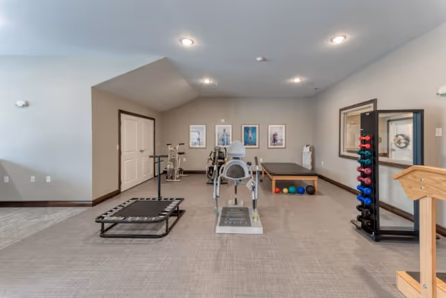 Spacious indoor exercise room with fitness equipment including a recumbent bike, mini trampoline, dumbbells, balance bench and exercise balls.