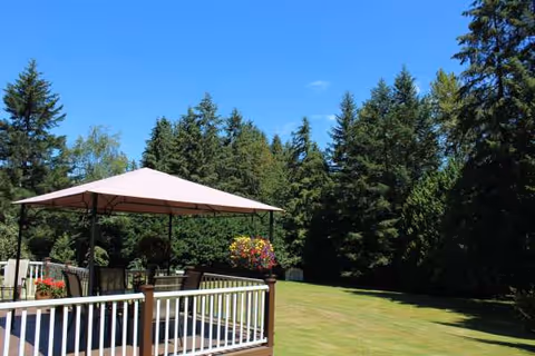 Outdoor deck with umbrella, railing, and manicured lawn framed by trees.