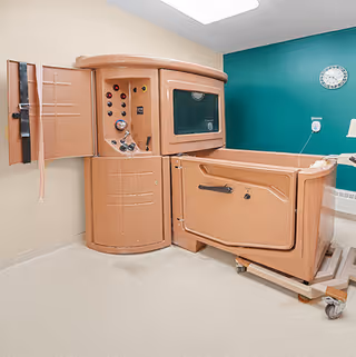 A peach-colored walk-in therapeutic bathtub and control unit in a clean bathing room with a teal accent wall and clock.