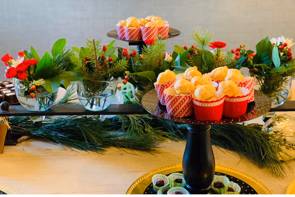 Tiered dessert stands with cupcakes surrounded by evergreen garlands and small floral arrangements on a table.