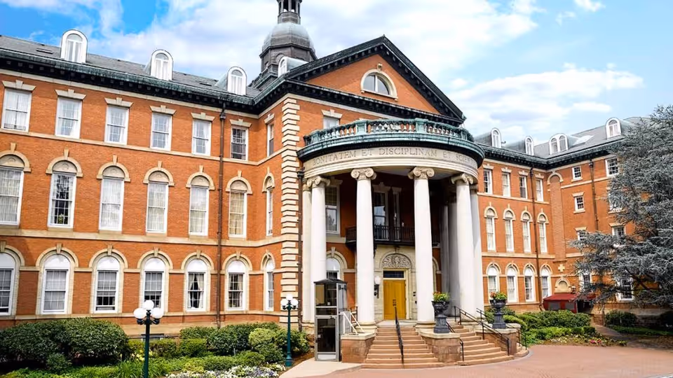 Grand red-brick building front with a columned circular portico, steps, and landscaped grounds.