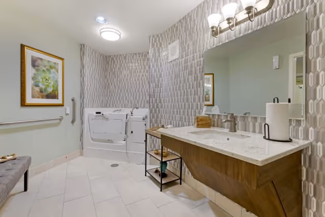 Accessible bathroom with a walk-in tub, floating vanity and sink, patterned accent wall, and a bench.