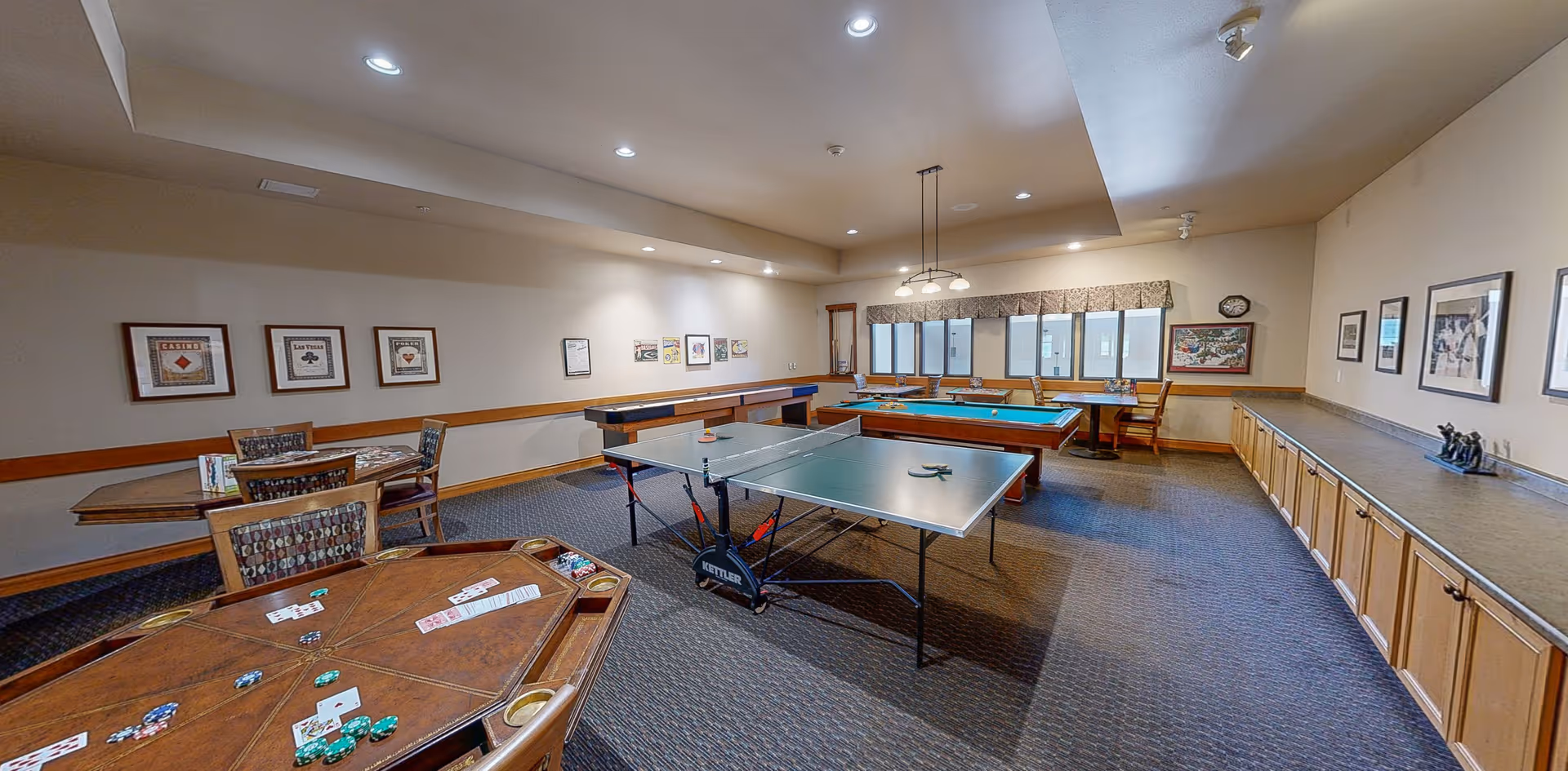 Spacious community recreation room with a poker table, ping-pong table, pool table and card tables under recessed lighting.