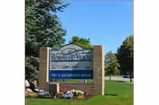 Brick entrance sign reading 'Rosewood Villas' with flowers, lawn and trees under a blue sky.