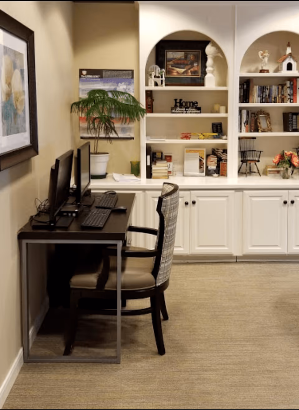 A computer workstation with two monitors and a chair in front of built-in white bookshelves and cabinets.