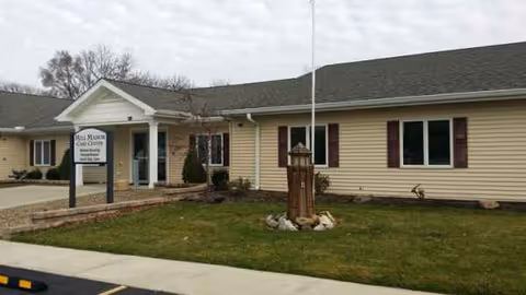 Single-story care facility with Mill Manor Care Center sign and manicured lawn at entrance.