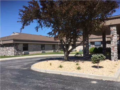 Exterior view of Willard Care Center showing driveway, tree, and stone columns.