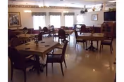 A dining room with multiple tables and chairs, place settings, large windows with valances, a TV and sideboard.
