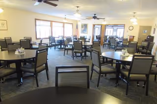 Spacious dining room with multiple round tables and chairs, ceiling fans, and large windows.