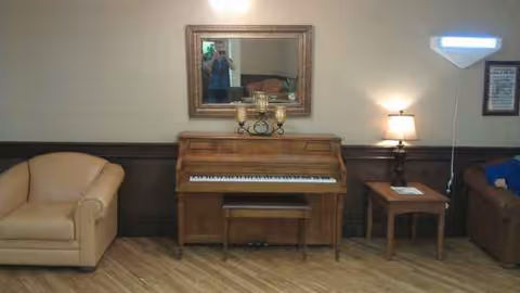 Upright piano centered between beige armchair and side table in a cozy lounge.