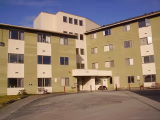 Front exterior of a multi-story assisted living building with a central covered entrance and paved driveway.