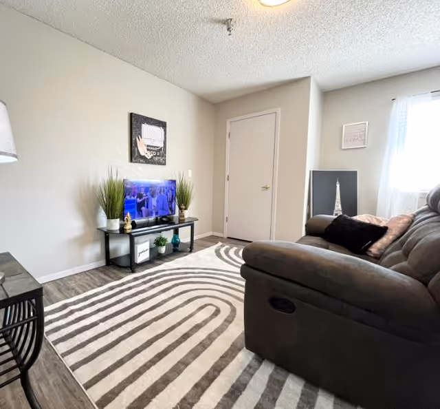 A cozy living room at Glade Avenue Assisted Living with TV, sofa, rug, and plants.
