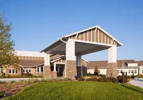 Front entrance of a senior living building with a covered porte-cochere and brick columns.
