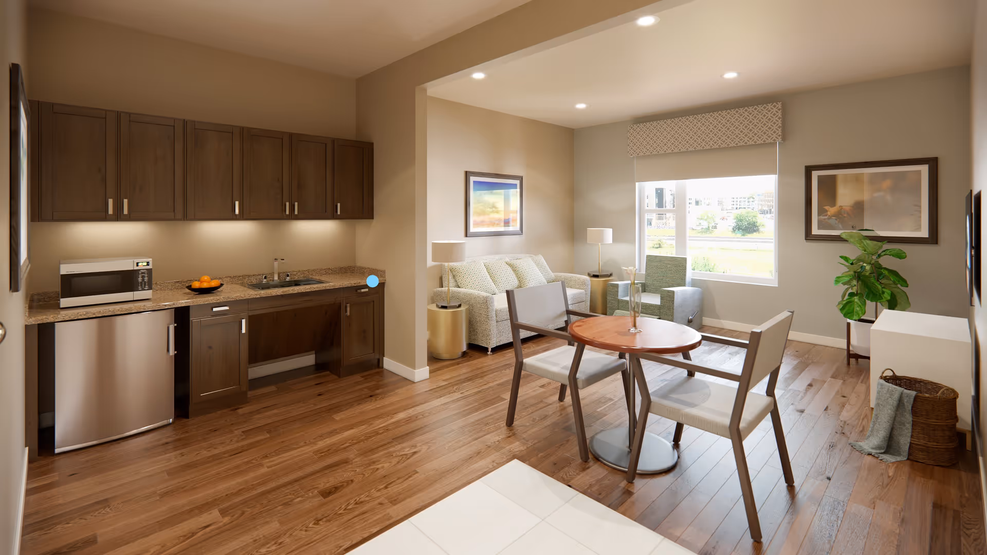 A cozy interior space featuring a small kitchen area with wooden cabinets, a microwave, a sink, and a dishwasher. Adjacent to the kitchen is a living area with a sofa, two armchairs, a round wooden table with two chairs, two side tables with lamps, framed artwork on the walls, a large window with a patterned valance, and a potted plant. The floor is a combination of wood and tile.