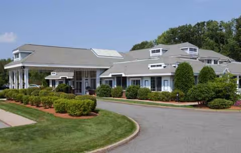 Exterior view of The Meadows senior living facility with manicured shrubs and curved driveway.