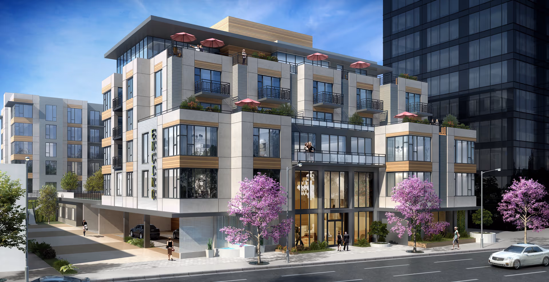 Modern multi-story residential building with balconies, rooftop terraces with red umbrellas, large windows, and landscaped surroundings including pink flowering trees. People are walking on the sidewalk and standing on balconies. The building has a sign that reads 'ENVISION'.