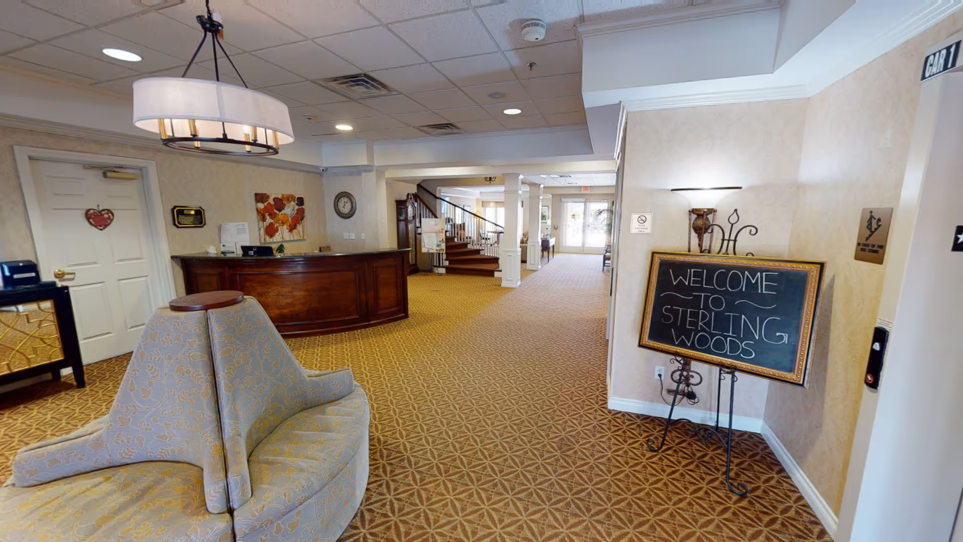 Lobby reception area with a curved front desk, seating, and a chalkboard sign reading "Welcome to Sterling Woods."