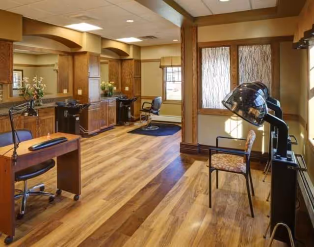 Interior salon area with chairs, mirrors, and hair dryers in a senior living facility.