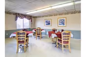 Small dining room with several tables covered in red and white tablecloths, wooden chairs, framed artwork on the wall and a window with a valance.