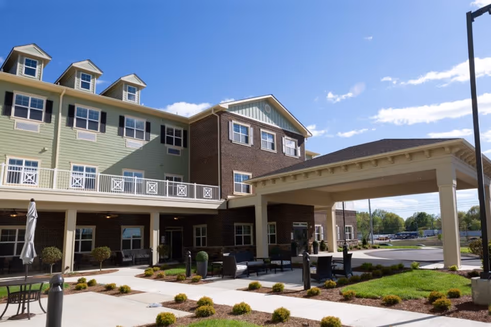 Exterior view of a senior living facility named Jubilee House with a covered entrance, outdoor seating area, and well-maintained landscaping under a clear blue sky.