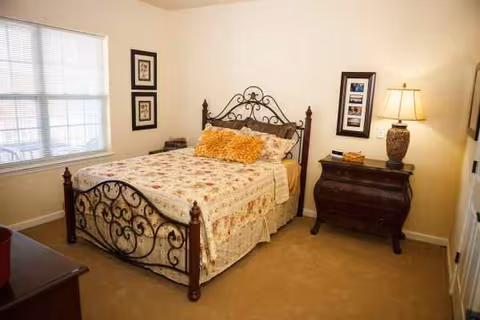 A cozy bedroom featuring a decorative wrought-iron bed, floral quilt, and bedside lamp.