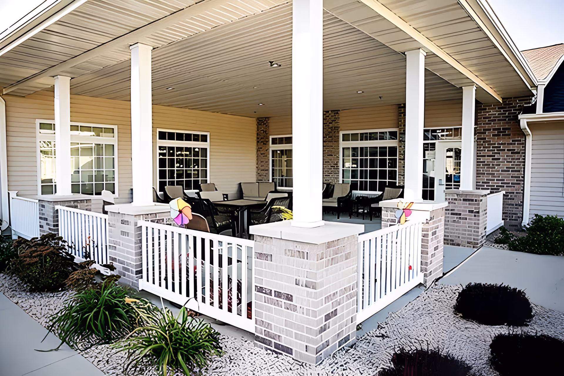 Covered exterior patio with white railings, columns, and seating at a senior living facility.