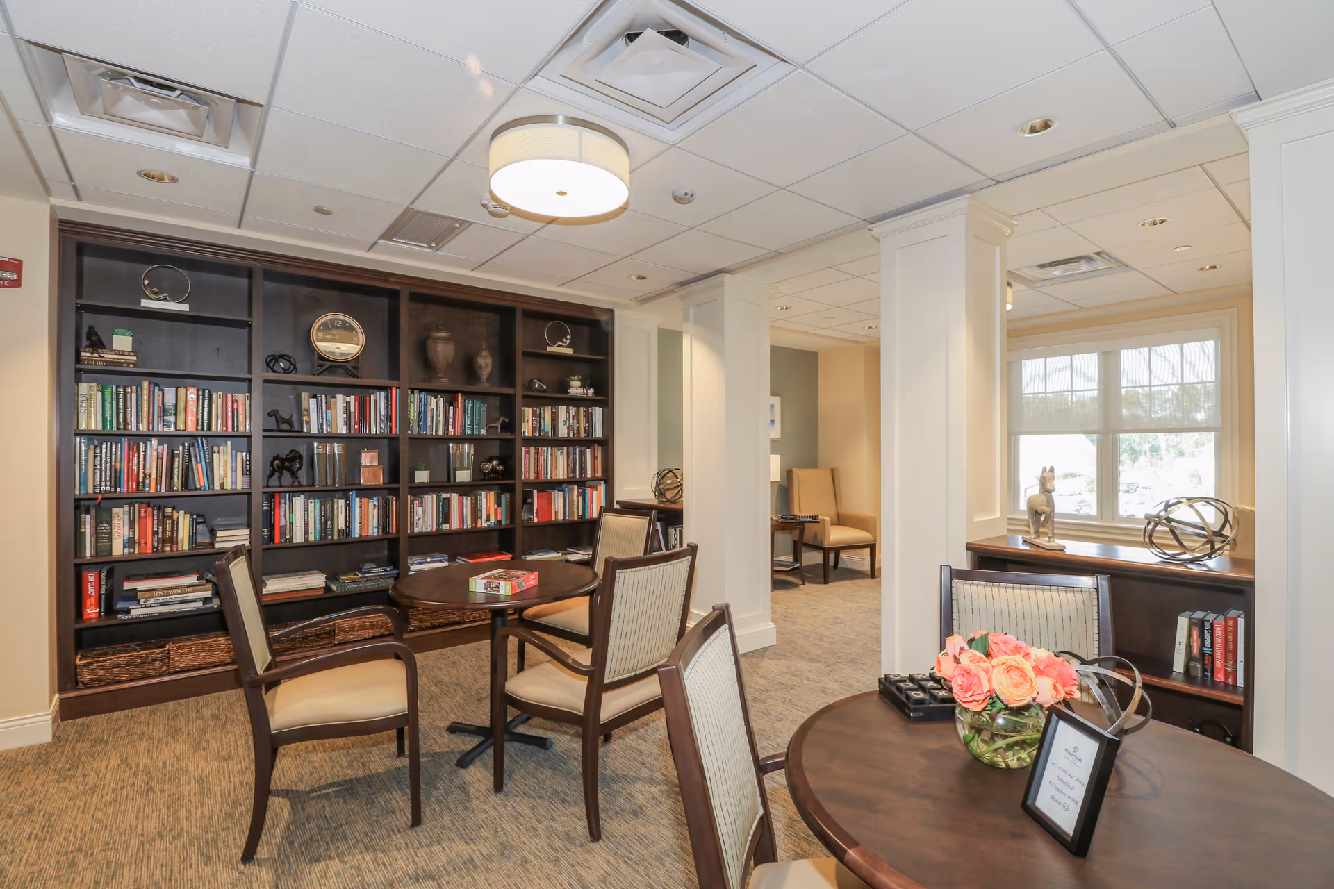 Bright communal lounge with bookshelves, round tables and chairs and decorative accents.