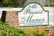 A brick-framed sign for Mt. Pleasant Manor sits near trimmed greenery.