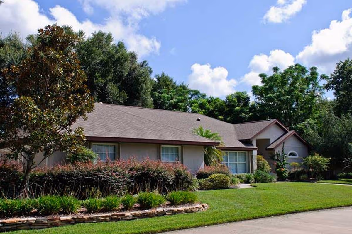 Single-story residential building with a manicured front lawn, shrubs, and trees under a blue sky.