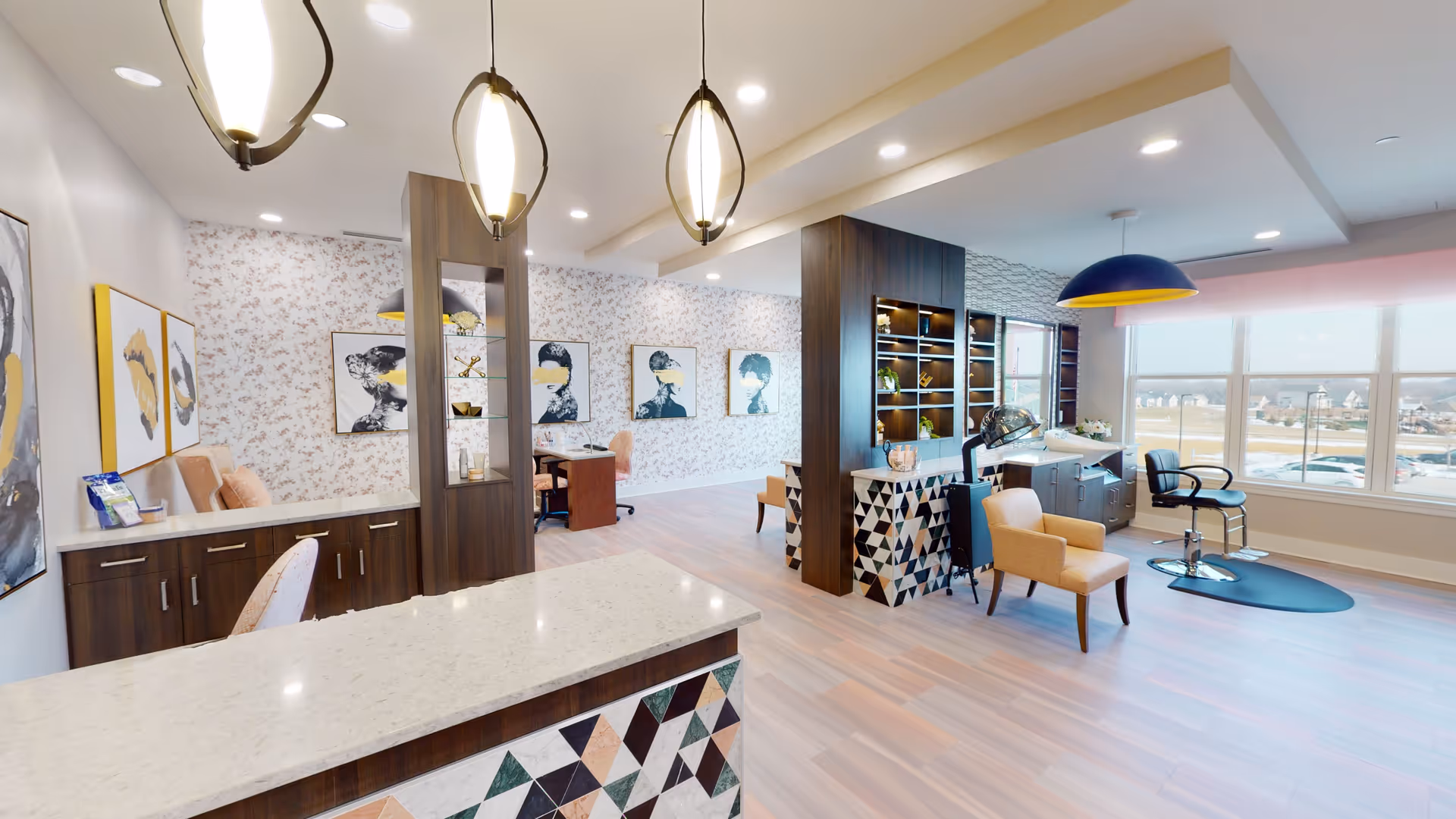A bright and modern interior space in CedarStone Senior Living featuring a reception desk with a geometric patterned front, three pendant lights hanging from the ceiling, comfortable seating including armchairs and office chairs, large windows letting in natural light, decorative wall art, and built-in shelving with plants and decor items.