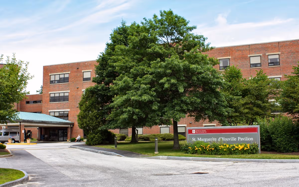 Exterior front of a brick senior living facility with trees, a driveway, and a sign reading 'St. Marguerite d'Youville Pavilion'.
