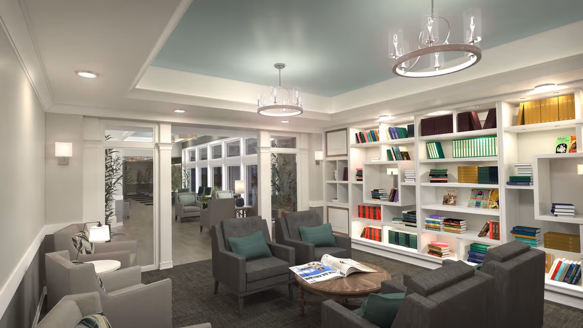 Well-lit communal lounge with bookshelves lining one wall, several armchairs and a coffee table with magazines.