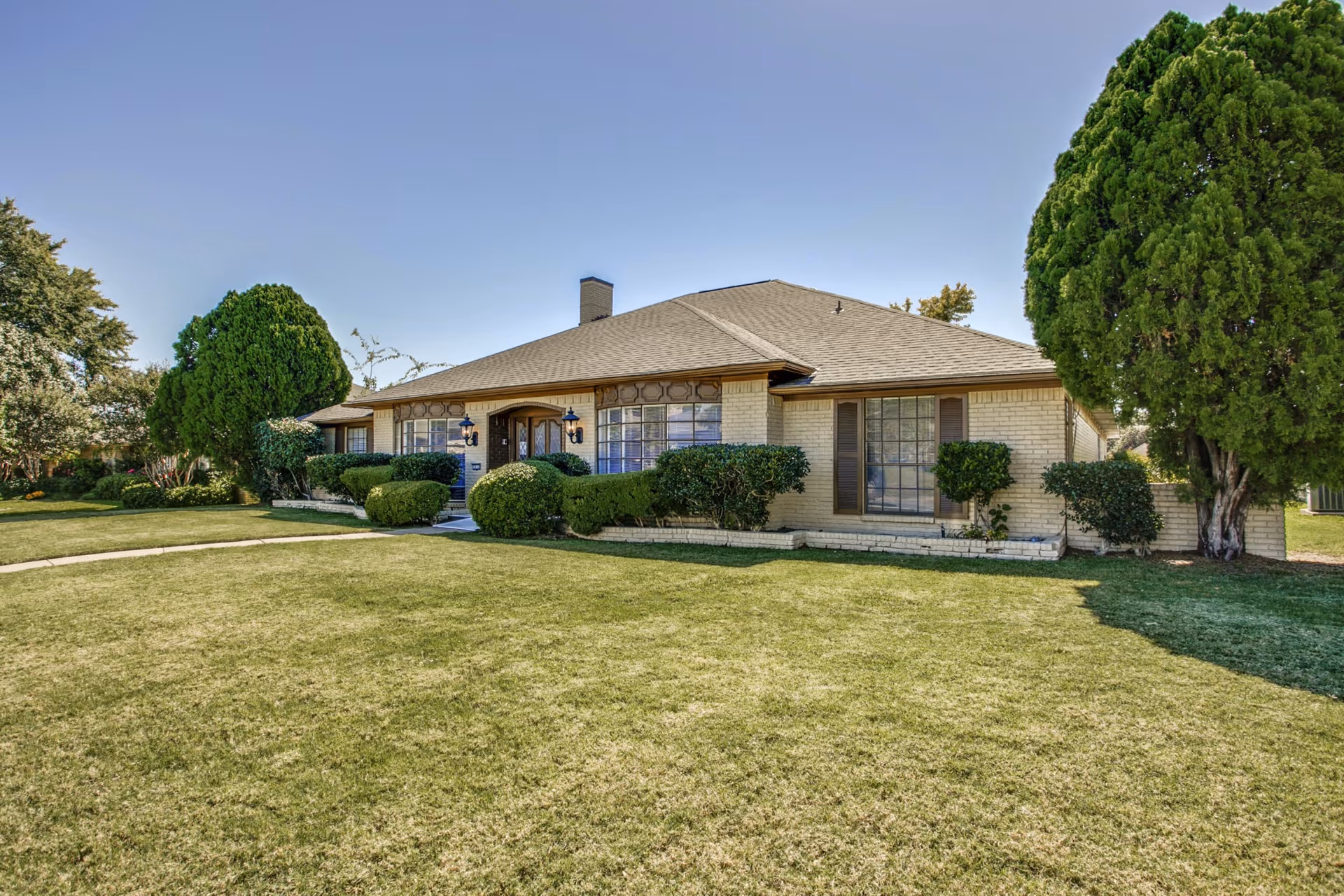 Single-story brick building with a large front lawn, trimmed shrubs, and a central entrance under a clear sky.