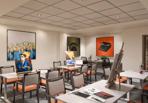 Bright interior activity room with tables, chairs, easels and colorful artwork on the walls.