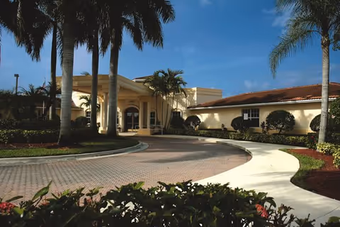 Sunlit HarborChase of Coral Springs entrance with curved driveway and palm trees.