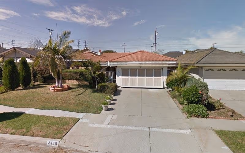 Front view of a single-story home with a driveway, yard, and palm tree.