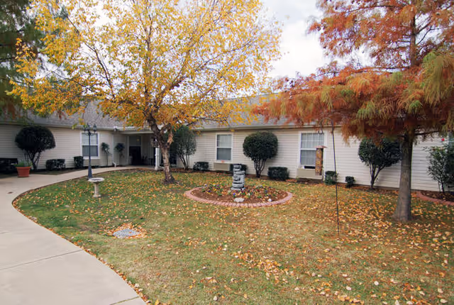 Single-story senior living building with a central courtyard, autumn trees, a small circular flowerbed and a walkway leading to the entrance.