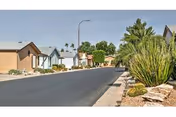 Paved street lined with single-story homes, desert landscaping, and palm trees under a clear sky.