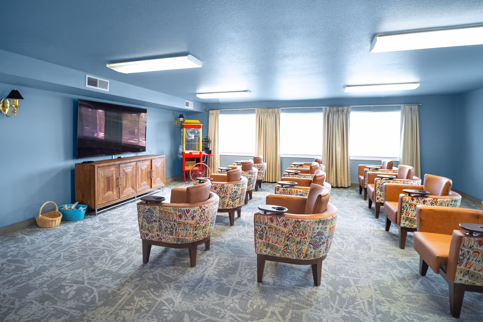 Bright communal lounge with rows of patterned and leather armchairs facing a large wall-mounted TV and a popcorn machine.
