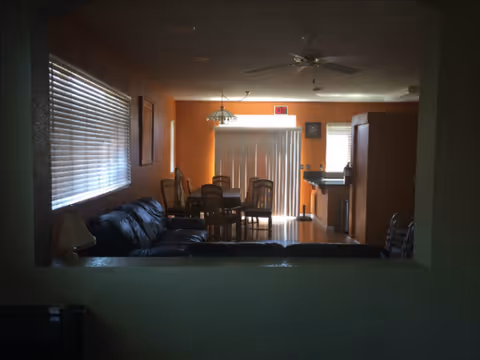 Interior living area with a sofa, dining table, and orange-walled kitchen in back.