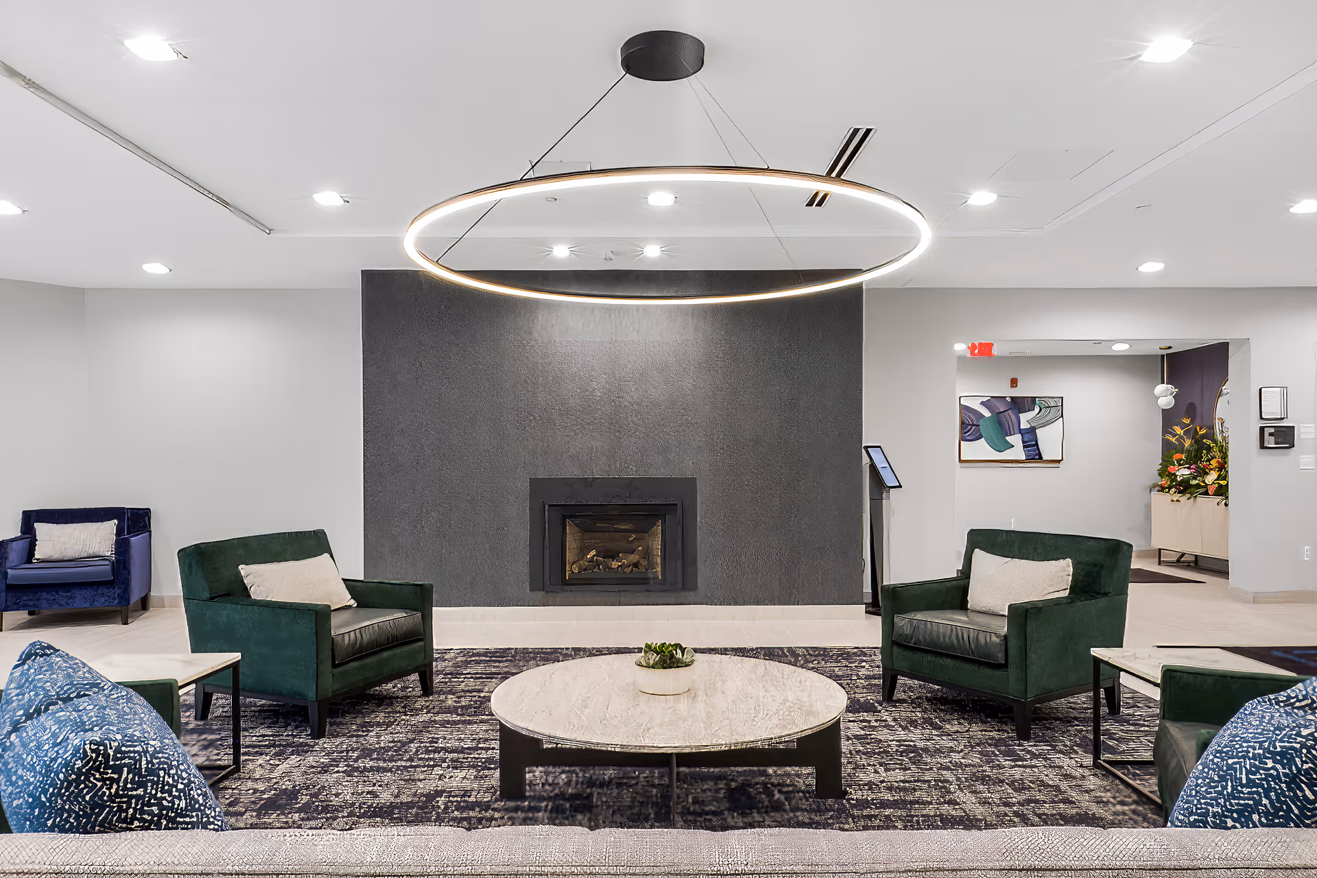 Communal lounge featuring a circular chandelier above a fireplace, green armchairs, and a round coffee table.